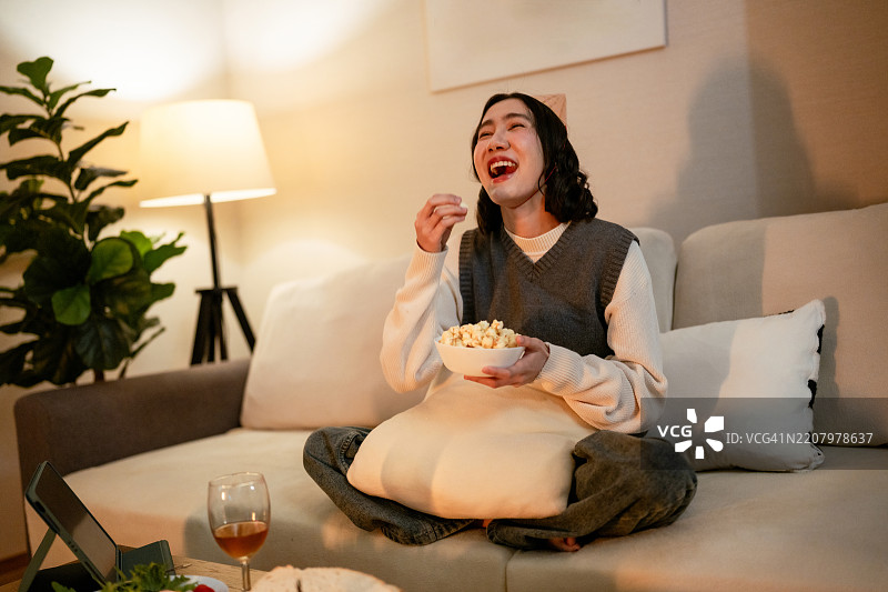 女人在沙发上放松，享受她最喜欢的节目，边吃爆米花，等待新年的倒计时。图片素材