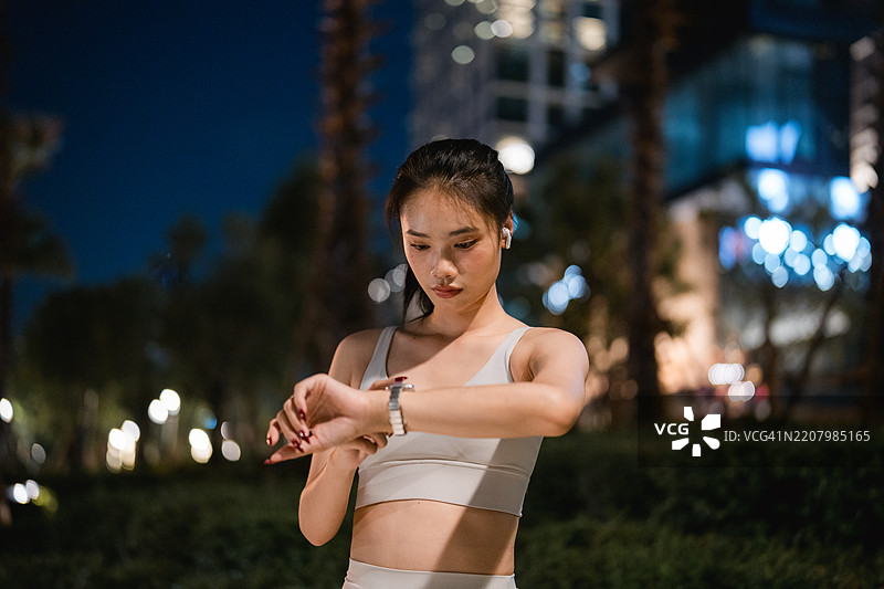 年轻女性在夜跑后停下来喘口气，查看智能手表上的进度图片素材