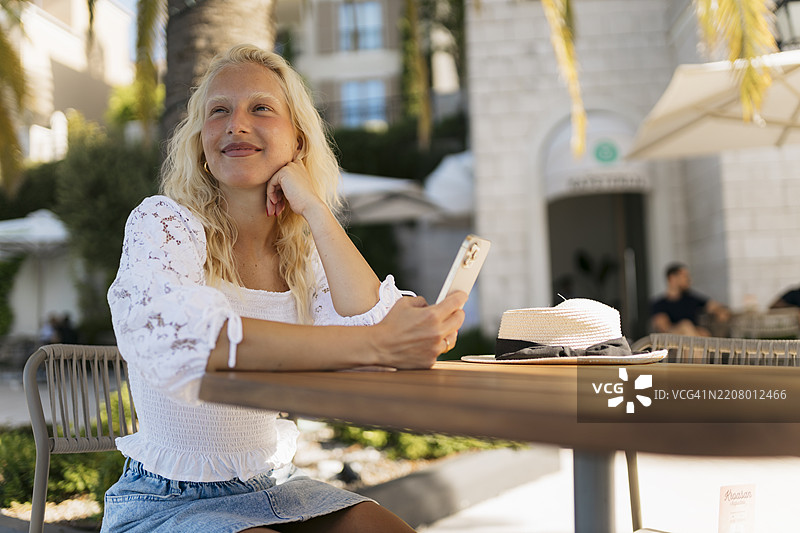年轻漂亮的女性坐在户外咖啡馆里玩手机图片素材