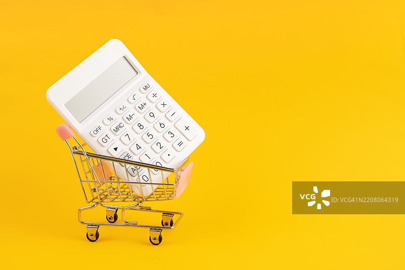 黄色背景上的购物车里的白色计算器。图片素材