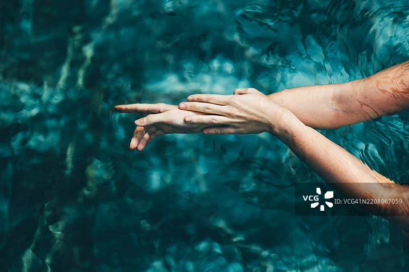 女人的手臂漂浮在泳池中。图片素材