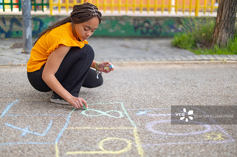 小女孩在路面上用粉笔画跳房子游戏图片素材