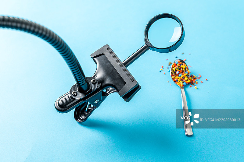 放大镜下蓝色背景上的勺子上的微塑料图片素材