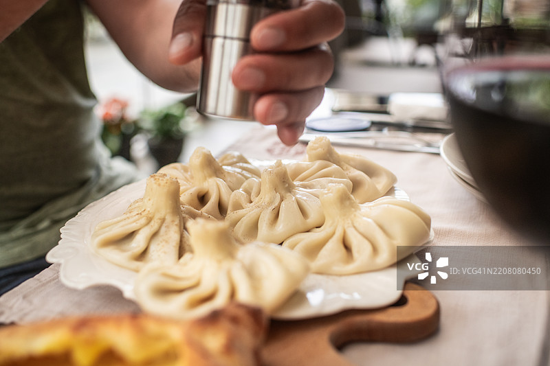 男人正在享用哈欣卡利 - 美味的肉馅饺子，配有香草和香料。传统的格鲁吉亚美食。图片素材