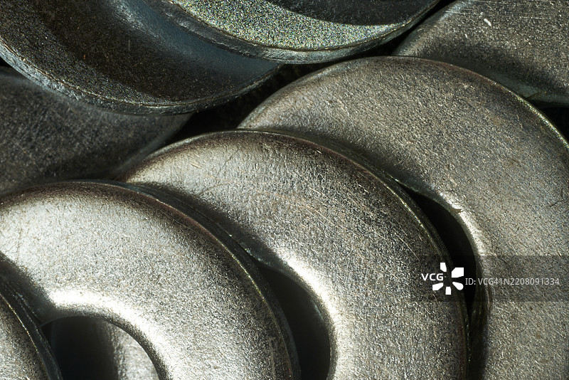 金属垫圈以几何排列相互交错，投射出复杂的阴影，并在精确重叠的圆形表面上反射光线。图片素材