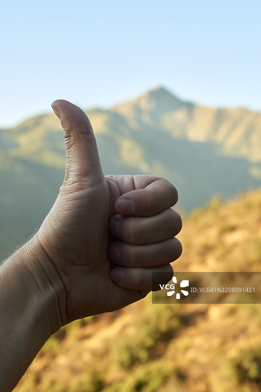 登山者在壮丽的山峰附近竖起大拇指，阳光照耀着岩石景观，表达在艰难的荒野徒步旅行后的胜利感。图片素材