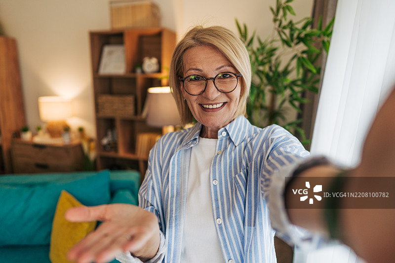 一位老年女性在家中进行视频通话，并伸出手来。图片素材