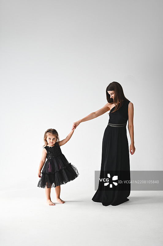 母女俩穿着优雅的黑色连衣裙，手牵着手。图片素材