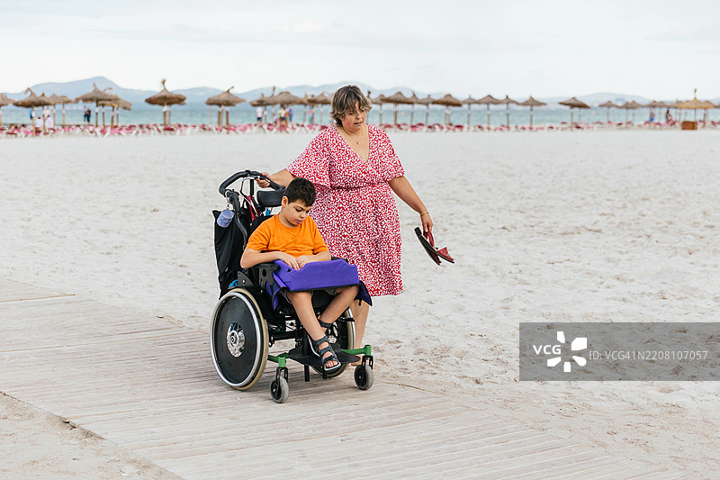 母亲在海滩上推着坐在轮椅里的脑瘫儿子图片素材