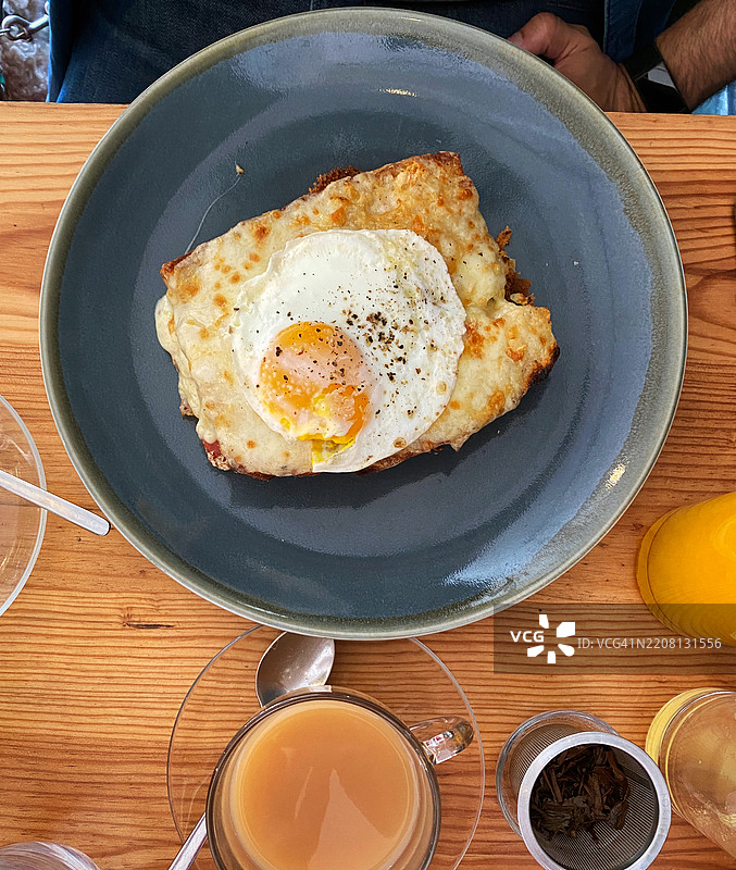 时尚的霍克斯顿咖啡馆里，丰盛的复活节早午餐在耶稣受难日享用。法式火腿奶酪三明治配有有机鸡蛋、手工酸面包和瑞士奶酪。融化的格鲁耶尔奶酪。庆祝早餐。搭配燕麦奶咖啡和新鲜橙汁，时间是2025年4月。图片素材