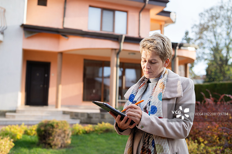 专注的女性在房子前做笔记图片素材