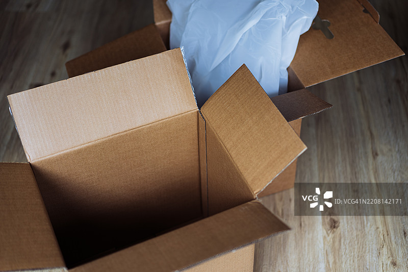 打开的纸箱放在木地板上，旁边有包装材料图片素材
