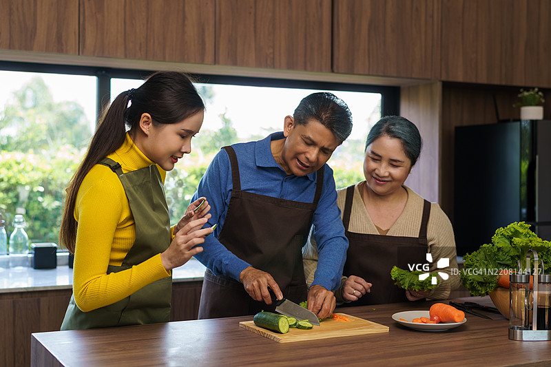 老年父母和女儿在厨房一起切菜准备食物。加强家庭关系的概念。图片素材