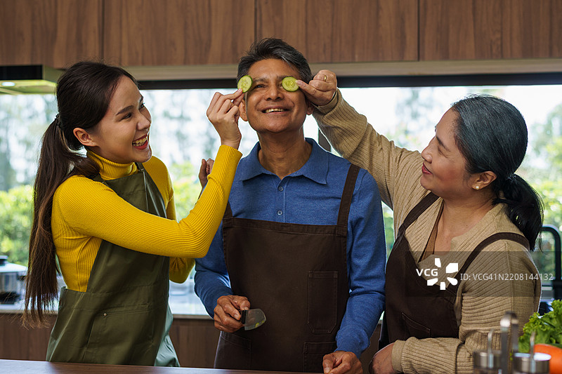 老年父母和女儿在厨房一起切菜准备食物。加强家庭关系的概念。图片素材