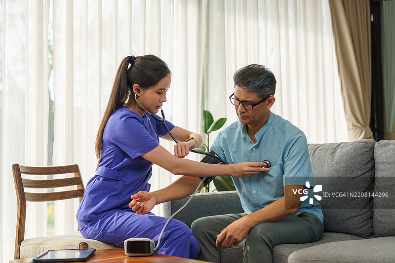 一位家庭健康护理专业人员在老年人的家中测量血压，并为他提供健康护理建议。图片素材