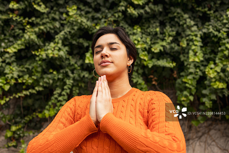 放松的女性双手合十，靠在常春藤墙上冥想图片素材