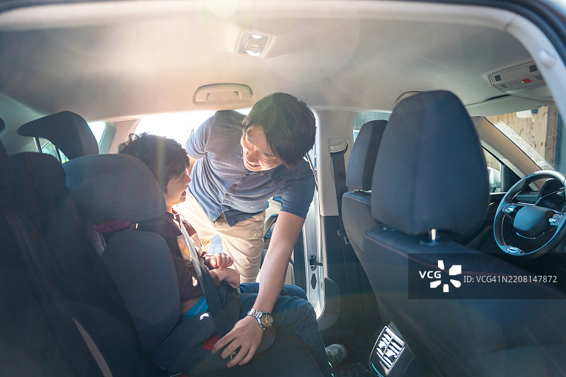 亚洲父亲在阳光明媚的早晨驾驶时帮助年轻儿子确保汽车座椅安全图片素材