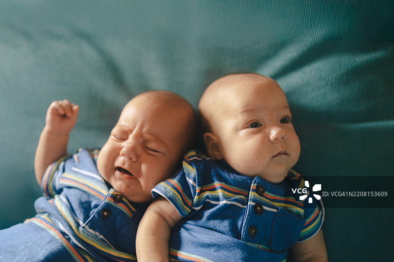 两个婴儿躺在沙发上：一个在哭泣，另一个很平静图片素材