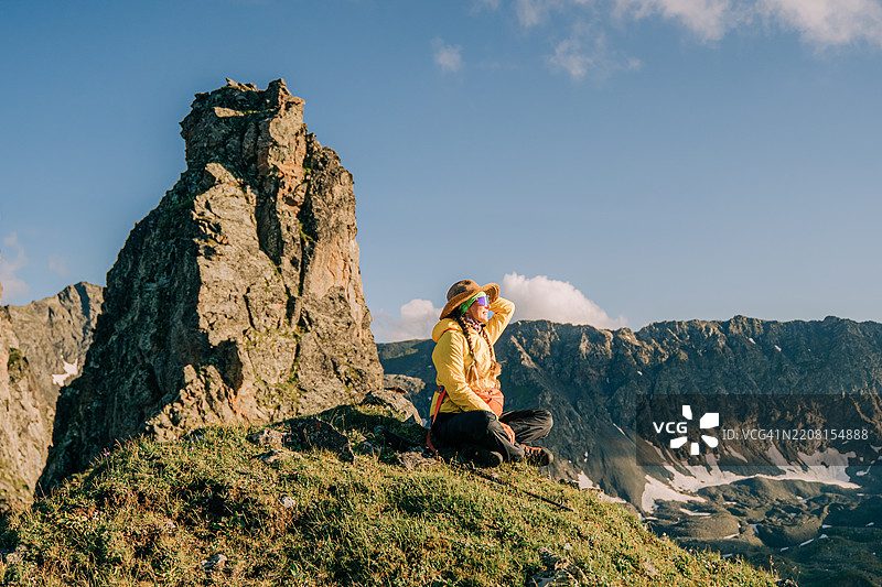女性徒步旅行者在夏日的阳光下休息，欣赏壮丽的山景图片素材