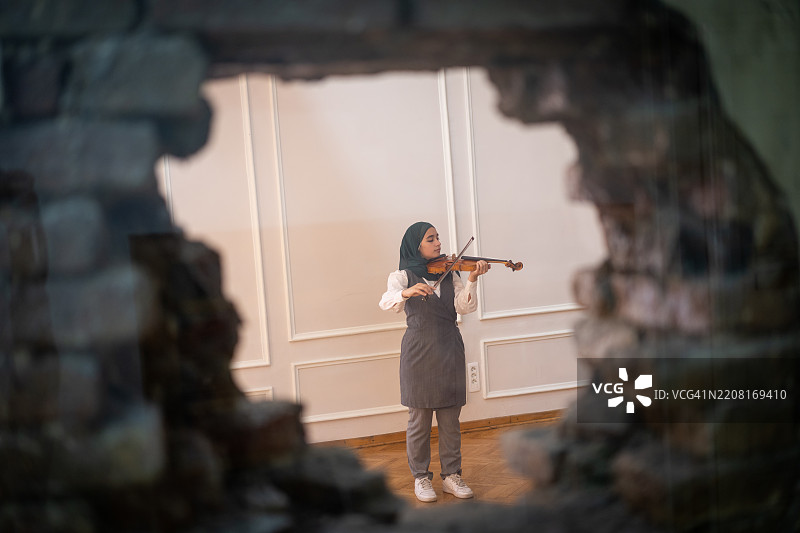 戴着头巾的阿拉伯年轻女性在拉小提琴图片素材