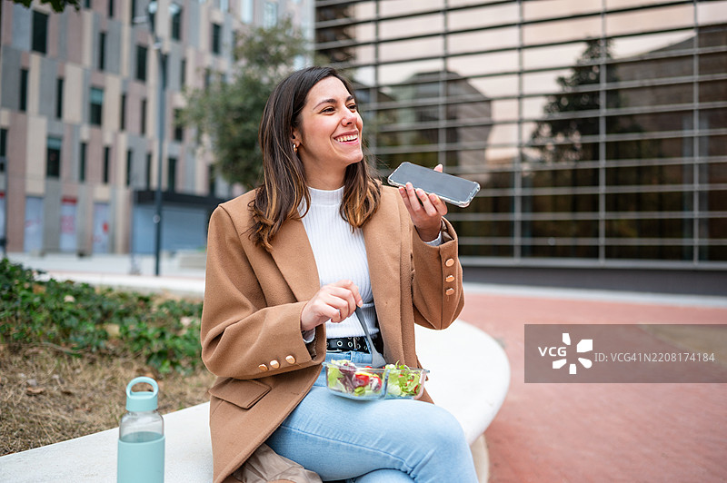 商务女性在户外吃沙拉并打电话图片素材