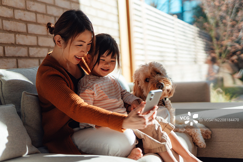 快乐的年轻亚洲母亲和女儿在家一起玩手机，享受乐趣图片素材