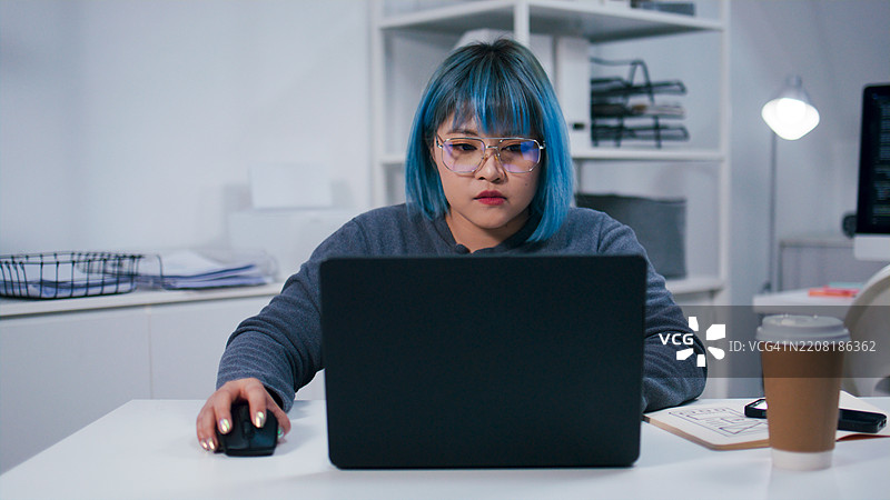 年轻的亚洲女性程序员在办公室夜间使用笔记本电脑编写代码，进行软件开发工作图片素材