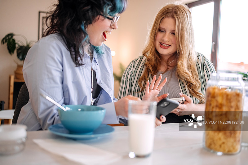 青少年女孩在家一起吃早餐，同时使用手机图片素材