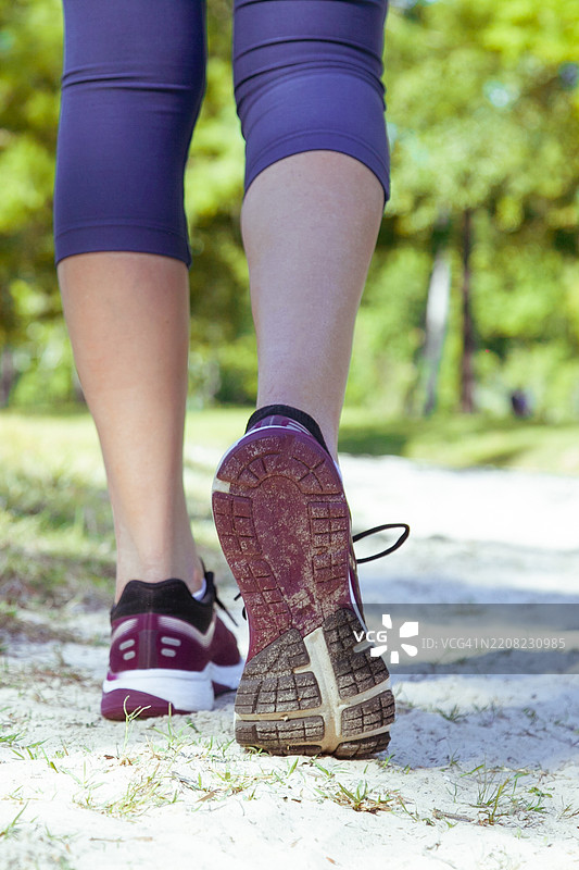女性穿着运动鞋在森林小径上行走的特写。积极的生活方式、户外健身和健康意识。图片素材
