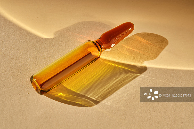 一个装有化妆品或医疗产品的安瓿瓶，背景为米色，散发着美丽的金色光芒。图片素材