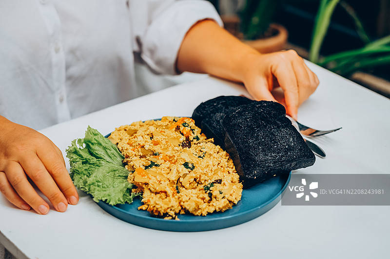 美味的早餐，蓝色盘子里有炒鸡蛋和炭烤吐司。女性享用健康的素食早餐。图片素材