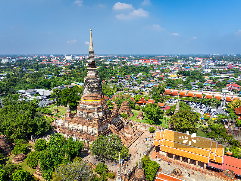 游客们在泰国阿育他耶历史公园参观壮观的古老瓦雅猜蒙空寺的鸟瞰侧视图,寺内的大佛塔矗立在较小的建筑群中,背景是现代城市的景象。图片素材