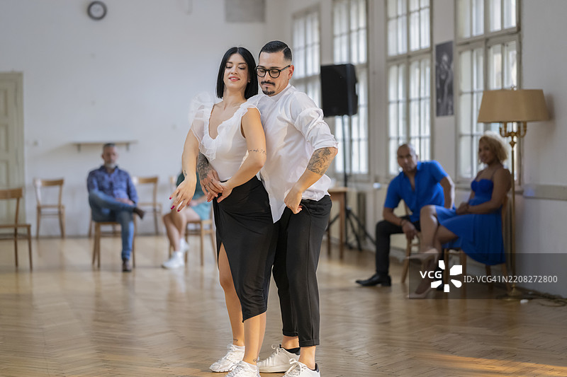 白人情侣在明亮的舞蹈工作室中优雅地跳舞，背景中有观众。图片素材