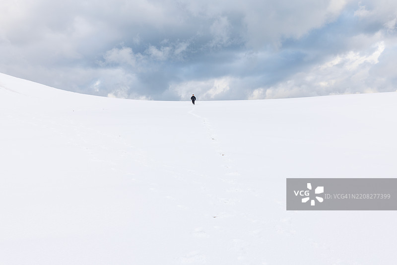 一位亚洲男性旅行者在雪中漫步，探索鸟取沙丘，沙丘被雪覆盖，天空美丽。图片素材