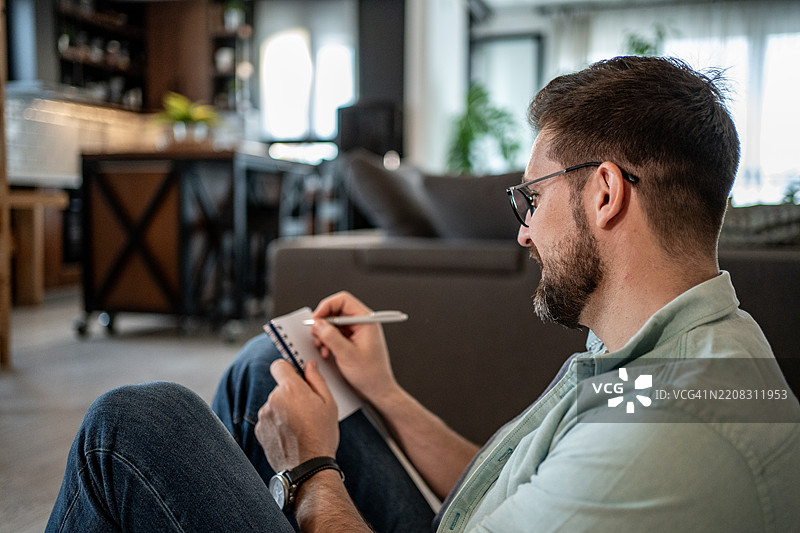 年轻男子坐在客厅地板上做笔记图片素材