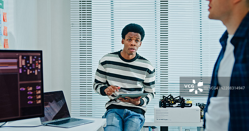 两名男性软件开发人员在办公室的桌子旁讨论项目编码，使用数字平板电脑。人工智能与编程。图片素材