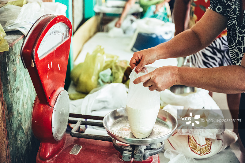 女性市场摊贩在市场上使用旧机械秤称量木薯粉图片素材