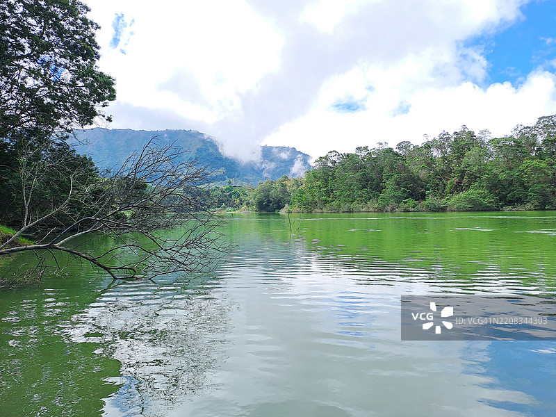 绿色湖泊（Telaga Warna / Warna Lake）与山脉、蓝天和云彩背景相映成趣图片素材