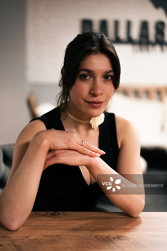 年轻女性坐在桌子旁，双手交叠，注视着镜头图片素材