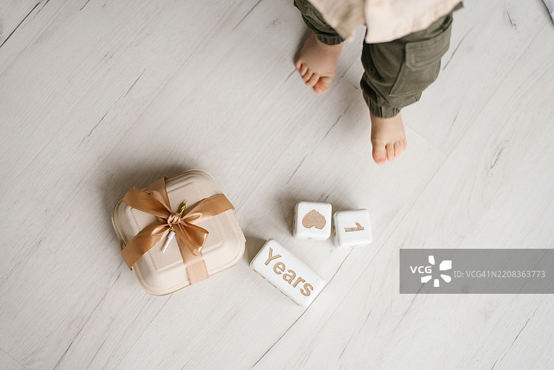 儿童生日蛋糕盒放在地上，旁边有一个写着“一岁”的盒子。孩子站在礼物旁边，正看着它。美国华盛顿州西雅图。图片素材
