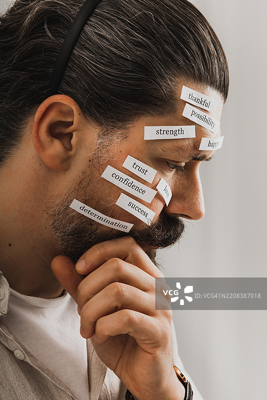 专注于一个男人面孔的肖像，面部装饰着代表情感和特质的文字标签。这个概念展示强调了爱、信任、自信和决心等积极价值观，体现了个人成长的主题。图片素材
