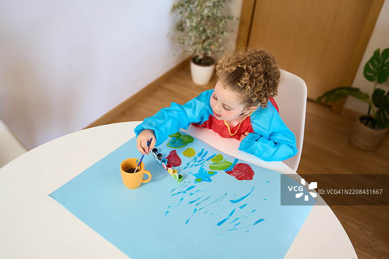 小女孩在家用水粉颜料在蓝色纸上画画图片素材