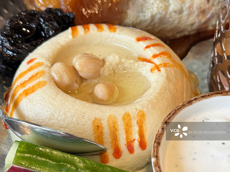 黎巴嫩小吃全景图，开胃菜自助拼盘，包含鹰嘴豆泥、茄子泥、枣、杏干、切片甜菜和黄瓜、希腊酸奶酱的小碗、金属勺，俯视角度，重点突出前景。图片素材