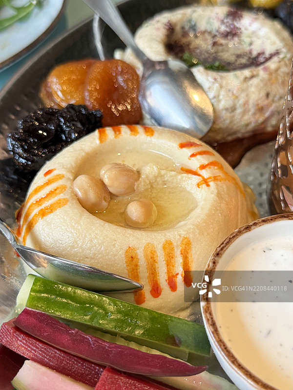 黎巴嫩小吃特写，开胃菜自助拼盘，包括鹰嘴豆泥、茄子酱、枣、杏干、切片甜菜和黄瓜、希腊酸奶酱的小碗、金属勺子，俯视角度，重点在前景。图片素材