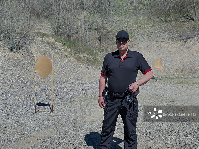 手持手枪、佩戴枪套的男子在户外射击场进行IPSC射击训练，目标靶在前。图片素材