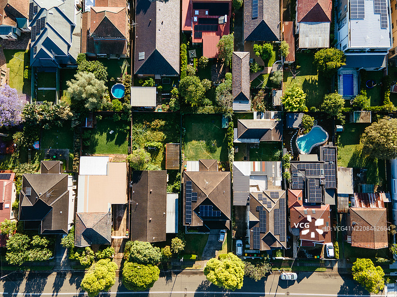 郊区社区的鸟瞰图，屋顶上装有太阳能电池板，游泳池被郁郁葱葱的树木和房屋环绕。图片素材