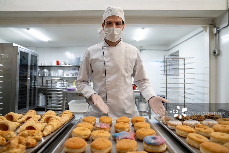 在工业面包店工作的面包师傅展示一些甜甜圈和糕点图片素材