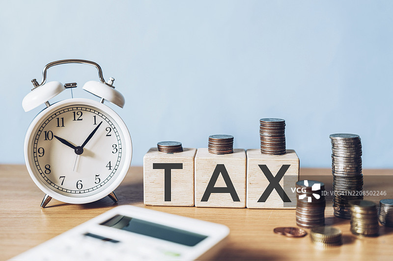 写在木块上的税务文字与堆叠的硬币图片素材