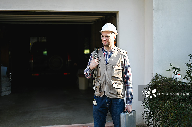 技术人员手持电缆和工具箱走出车库图片素材