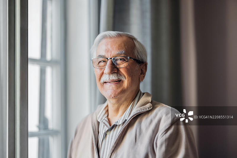 微笑的老年男子站在明亮房间的窗边图片素材